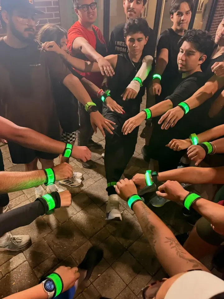 Hands in, everyone wearing green light-up wristbands
